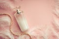 Women`s perfume on a delicate pink background with feathers