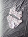 Women`s pink gentle sexy lingerie lying at grey bed as background. Vertical photo