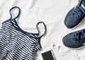 Women`s sports clothing on a light background. Sports women`s tank top with thin spaghetti straps, striped, running sneakers, ph