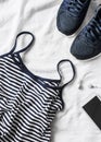 Women`s sports clothing on a light background. Sports women`s tank top with thin spaghetti straps, striped, running sneakers, ph