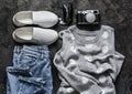 Women`s spring clothes - mom`s jeans, grey polka dot pullover, sneakers, headphones and vintage camera on a dark background, top Royalty Free Stock Photo