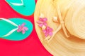 Women`s straw hat pink tropical flowers turquoise slippers sea shells on bright coral crimson background. Beach vacation fashion