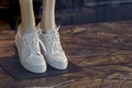 Women`s white sneakers with a shiny inset along the contour on the legs of a mannequin in a shop window. Background