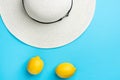 Women`s white straw beach hat ripe organic yellow lemons on mint blue background. Summer vacation fun fashion