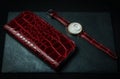 Women`s white wristwatch with a handmade strap made of genuine red crocodile leather with a red leather wallet on a dark