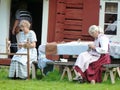 Women sewing dressed in old costumes outside old red barn in Sweden