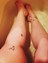 Women sitting in a low water bath with black ink tattoos covering her legs