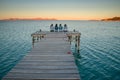 Women sitting together on the wooden pier in beautiful summer sunrise light. Playa de Muro, Mallorca