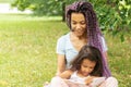 A woman teaches a girl to read on the grass in nature, mother and daughter in the park read a book, african happy family spend