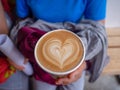 Women tourists wear a blue shirt hold hand a coffee art with heart-shape pattern.Close up cup of coffee with heart-shape pattern
