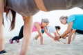 Women of various ages doing fitness workouts in class exercise with coach on beach. Ladies doing paired plank exercises