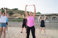 Women of various ages doing fitness workouts in class exercise with coach on the beach. Ladies working with resistance