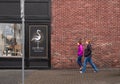 Women walking fast on the brick wall background in town. Urban infrastructure, people walking on a street in springtime