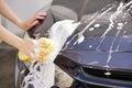 Women washing a soapy grey car with a yellow sponge.