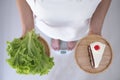 Women weigh themselves on scales and holding vegetables and chocolate cakes. Vegetables are useful to the body and the cake has Royalty Free Stock Photo