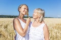 Women in a wheat field. An adult daughter with an elderly mother in white dresses are holding spikelets in their hands on a bright Royalty Free Stock Photo