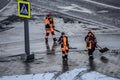 Women workers in orange uniforms with snow shovels walk down the street