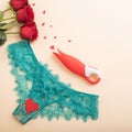 Women's green lace panties, a bouquet of scarlet roses, a clitoral vibrator and hearts on a beige background. Valentine