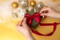 Women& x27;s hands tie a red ribbon on a green round gift. Christmas background with golden balls and angel hair Royalty Free Stock Photo