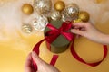 Women& x27;s hands tie a red ribbon on a green round gift. Christmas background with golden balls and angel hair Royalty Free Stock Photo