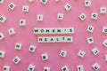 Women& x27;s Health word made of square letter word on pink background.