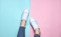 Women& x27;s legs in tight, torn jeans, sneakers on pink blue pastel background. Top view, minimalism