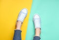 Women& x27;s legs in tight, torn jeans, sneakers on yellow blue pastel background. Top view, minimalism, copy space.