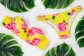 Women yellow swimsuit and green leaves of monstera on a white wooden background. Fashionable beachwear. Women`s swimming suit wit