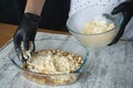 Womens black-gloved hands make apple crisp pie, put dough crumbs on grated apple