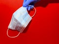 Womens hand in a blue gloves hold a medcine mask on a red background Royalty Free Stock Photo