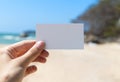 Womens hand holding blank white business greeting card on summer beach