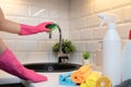 Womens hands cleaning kitchen tap on a black sink with rubber gloves and in front blurred cleaning products for disinfection Royalty Free Stock Photo