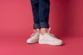 Womens legs jeans white sneakers street fashion studio pink background