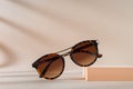 Womens Tortoiseshell frame sunglasses on a podium on a beige background with shadows. Trendy sunglasses still life in minimal