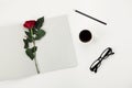 Womens working space with cup of coffee, pencil, empty notebook, glasses and rose flower on white table overhead view. Flat lay.