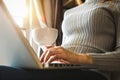 Womman using laptop and typing and holding coffee cup