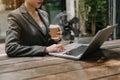 Womman using laptop and typing on laptop and holding coffee cup in cafe, home office