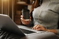 Womman using laptop and typing on laptop and holding coffee cup in cafe, home office