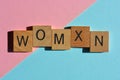 Womxn, in 3d wooden alphabet letters isolated on pink and blue background