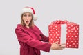 Wondered and amazed young woman in red coat and Christmas hat holding big box of present. Model looks on camera Royalty Free Stock Photo