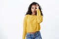 Wondered, amused dark-skinned girl with curly hairstyle, wear yellow sweater folding lips gasping wow as checking out