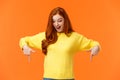 Wondered and excited, amused cute redhead woman in yellow sweater pointing fingers down, look bottom and smiling, check