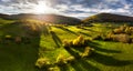 Wonderful autumn colored forest, setting sun with dramatic sky, valley with green grass and trees. Sunlight nature landscape