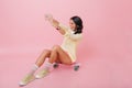 Wonderful brunette woman in yellow outfit sitting on skateboard in room with pink interior. Indoor portrait of dreamy Royalty Free Stock Photo