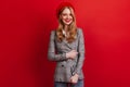 Wonderful french woman in jacket smiling at camera. Studio shot of romantic girl in beret isolated on red background