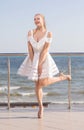 A wonderful lady posing on a terrace. A smiling female on a bright sky background. A stylish girl in a short white dress. Royalty Free Stock Photo