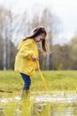Wonderful little girl standing in puddle on lawn and looking down with curiosity, spending autumn day in nature.
