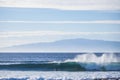 Big wave rolling it and crush at the beach with another tropical island in the background. Blue tones and sky for vacation and Royalty Free Stock Photo