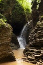 Wonderful stormy summer waterfall in canyon of layered rocks overgrown moss with lush green forest, bright splashes, sunbeams. Royalty Free Stock Photo