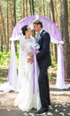 Wonderful stylish rich happy bride and groom standing at a wedding ceremony in green garden near purple arch with Royalty Free Stock Photo
